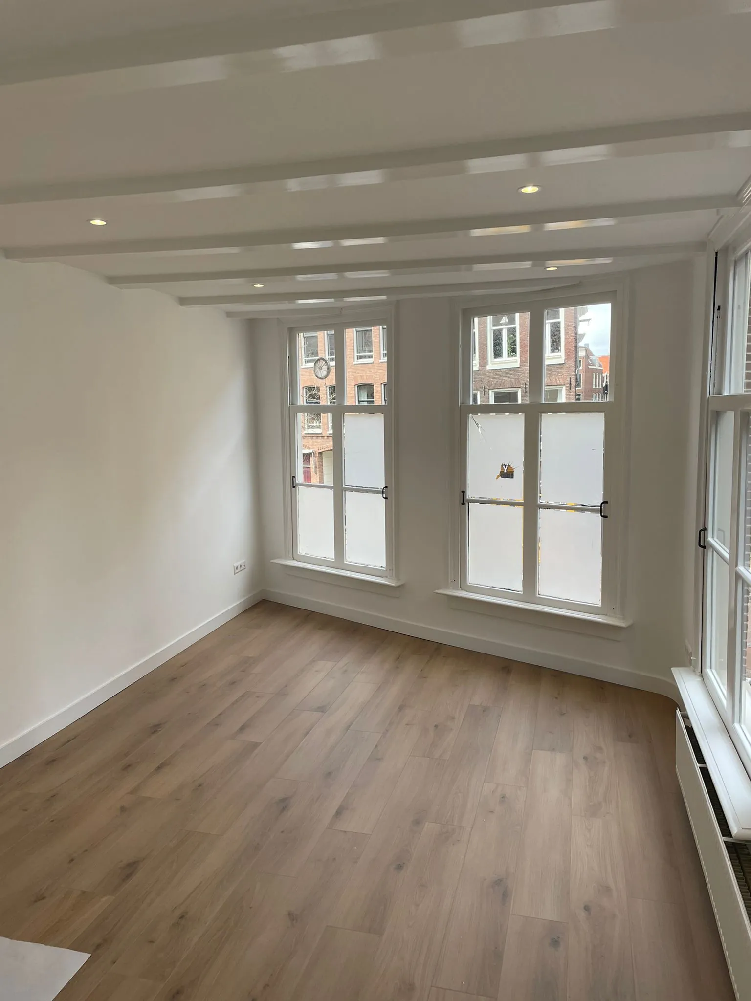 Licht en modern interieur van een lege kamer met houten vloer en grote ramen aan de Korte Kolksteeg.